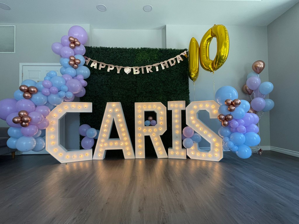 Green boxwood wall framed by balloon garlands with Markham marquee letters